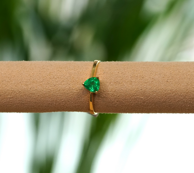 A gold ring with a pear-cut green gemstone displayed on a tan jewelry stand against a blurred green.background.